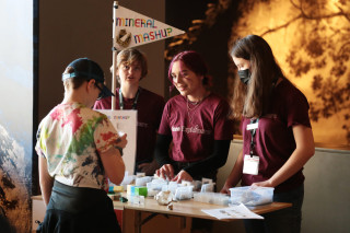 Teen explainers speak to a museum guest visiting their booth inside a gallery.